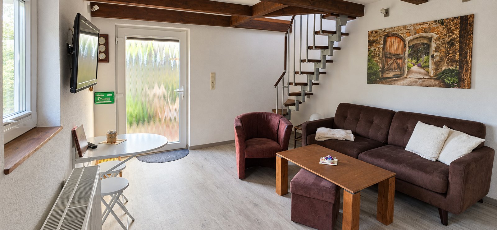 Wohnzimmer mit Sofa, Sessel, kleinem Esstisch und Wendeltreppe ins Obergeschoss